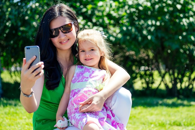 Beautiful brunette woman make selfie phone with children daughter in summer park