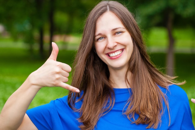 Beautiful brunette woman making a call me gesture summer outdoors