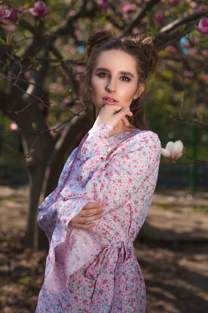 Beautiful brunette woman posing near the flowering magnolia tree in fashionable dress