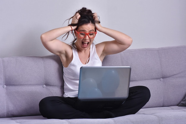 Beautiful brunette woman in red glasses on sofa using laptop