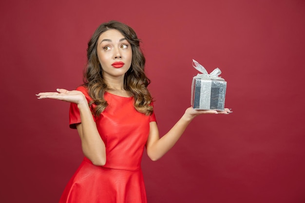 Beautiful brunette woman saddened by a gift in a red dress on a red background with copy space