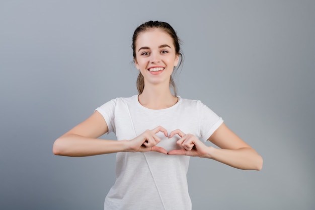 Beautiful brunette woman showing heart with hands isolated over grey