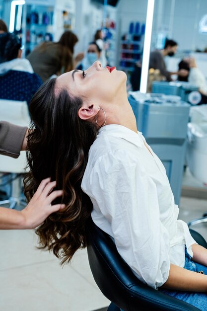 Beautiful brunette woman straighten her long gorgeous hair in a beauty salon