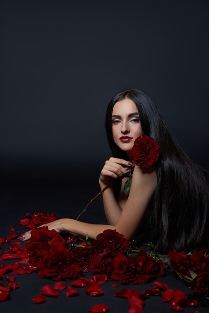 Beautiful brunette woman with a bouquet of rose flowers is sitting on the floor in a black bodysuit. Long hair, slim body