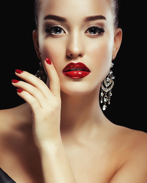 Beautiful brunette woman with bright makeup and jewelry earrings smiling closeup Red lips and nails evening makeup