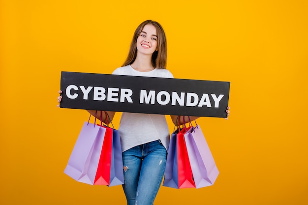 Beautiful brunette woman with colorful shopping bags and copyspace text cyber monday sign banner isolated over yellow