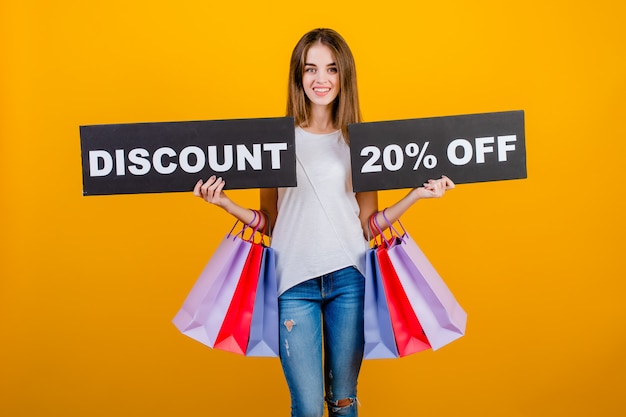 Beautiful brunette woman with colorful shopping bags and copyspace text discount 20% sign isolated over yellow