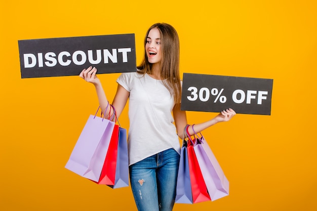 Beautiful brunette woman with colorful shopping bags and copyspace text discount 30% sign banner isolated over yellow