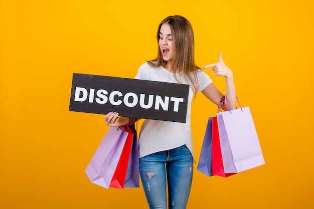 Beautiful brunette woman with colorful shopping bags and copyspace text discount sign banner isolated over yellow