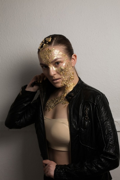 Beautiful brunette woman with creative makeup of golden foil on her face, hair and neck