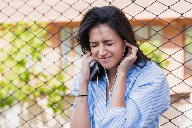 Beautiful brunette woman with earphones on the city street Young brunette smiling business woman holding ears of loud music Peoplelifestyle concept