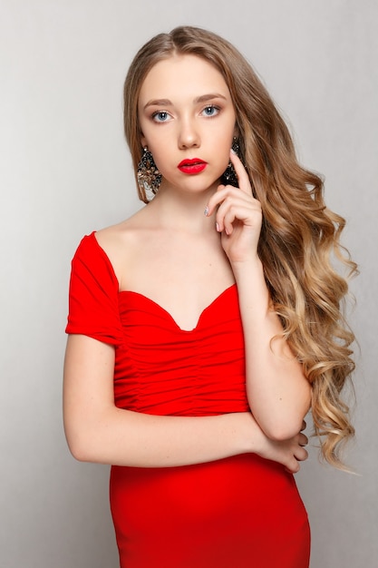 Beautiful brunette woman with long curled hair in a red dress wearing earrings.