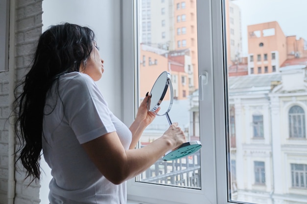 Beautiful brunette woman with long wavy hair admires herself in mirror