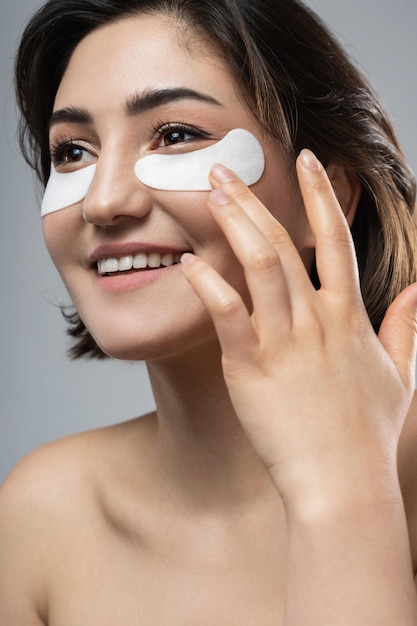 Photo beautiful brunette woman with a smooth skin applying adhesive undereyes patches for dark circles