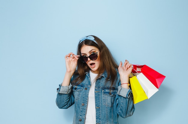 Beautiful brunette woman with sunglasses enjoys the shopping she has made on the blue background