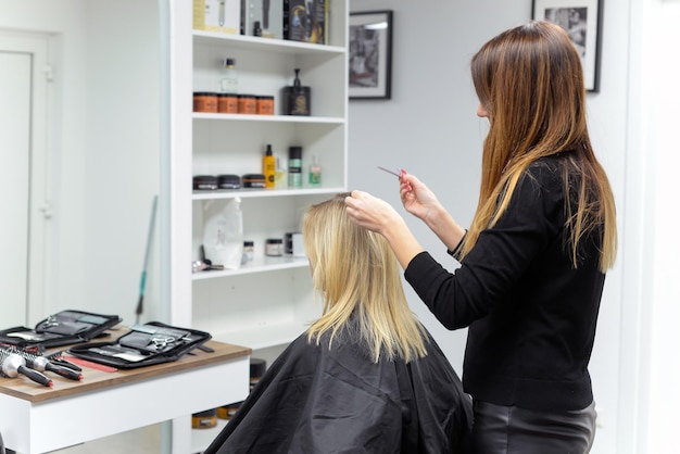 Beautiful brunette working as a hairdresser cuts the ends of the client's hair in a beauty salon