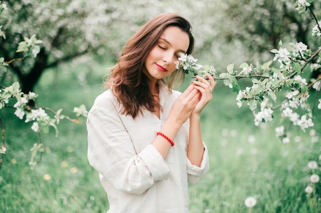 Beautiful brunette young girl with red lips posing in blooming apple trees in spring forest.