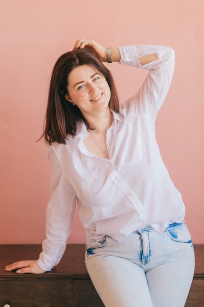 Beautiful brunette young woman relaxing and posing for camera on pink wall backgrorund.