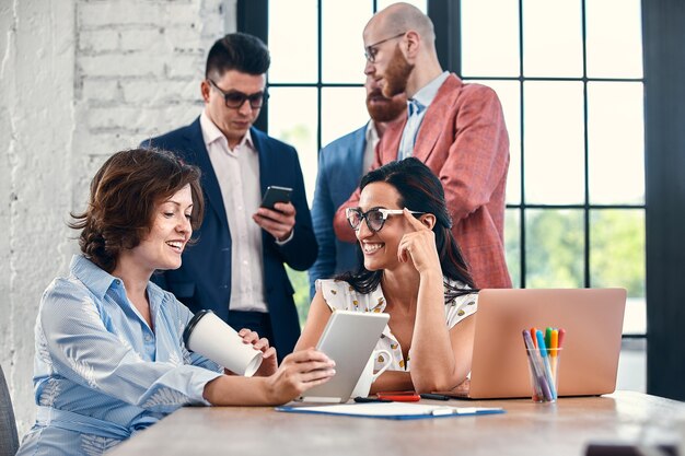 Beautiful business people are using gadgets, talking and smiling during the conference in office