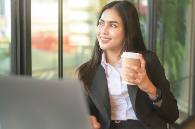 A beautiful business woman is analyzing financial data via computer , drinking coffee in coffee shop . business people lifestyle . technology concept .	
