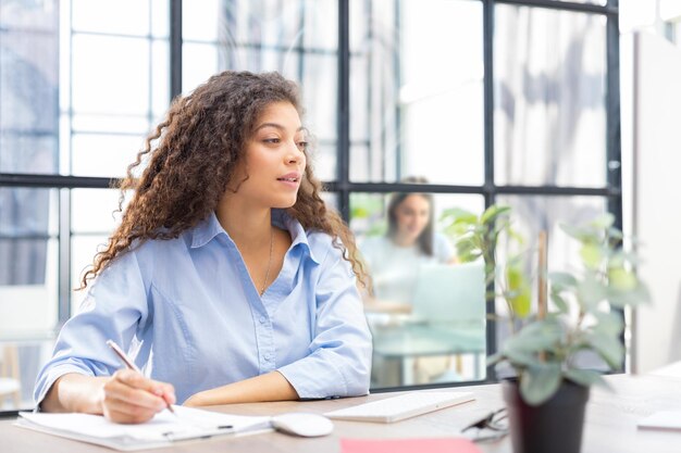 Beautiful business woman is examining documents while sitting in the office Collegue is on the background