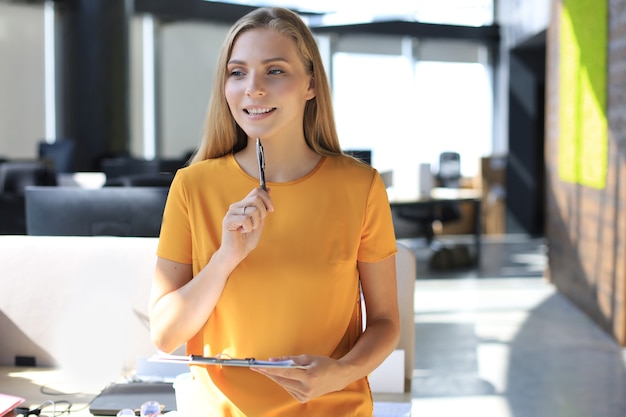 Beautiful business woman is smiling and writing something down while standing in the office.