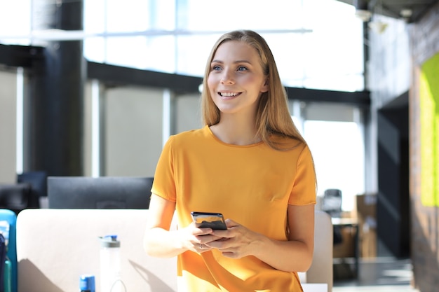 Beautiful business woman is using mobile phone while standing in the office.