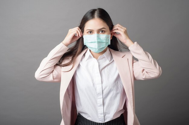 Beautiful business woman is wearing surgical mask on gray background