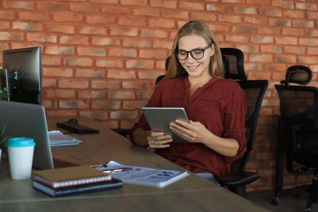 Foto la bella donna d'affari sta lavorando utilizzando la tavoletta digitale mentre è seduta in ufficio creativo.