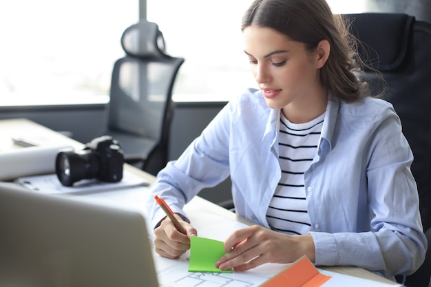 Beautiful business woman is writing something down while sitting in the office desk.