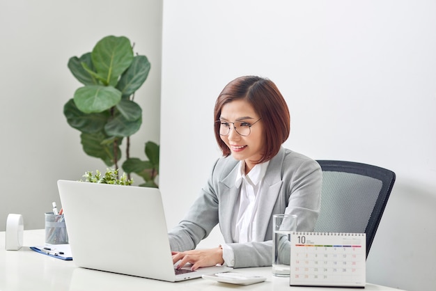 Beautiful business woman smile sitting at the desk working using laptop looking at screen typing on laptop over white background