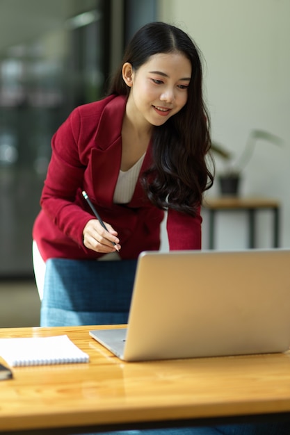 オフィスに立って、ラップトップコンピューターを介して彼女のプロジェクトに取り組んでいる美しいビジネスウーマン。