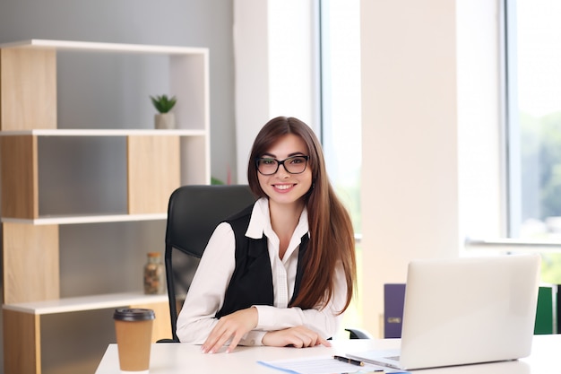 Beautiful business woman uses a laptop and smiles while working in the office