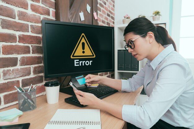 beautiful business woman using mobile cell phone paying through credit card e-commerce when her computer getting error problem.