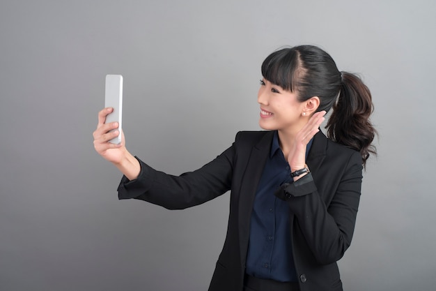 灰色の背景にスマートフォンを使用して美しいビジネス女性