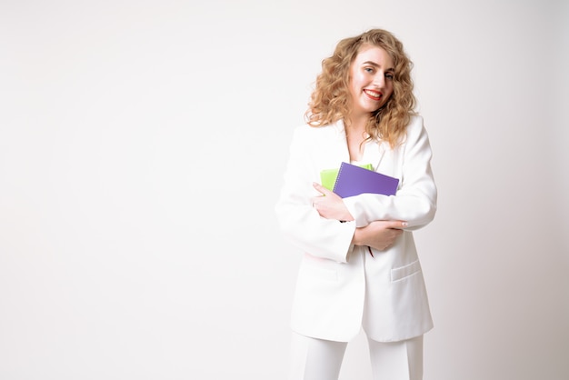 Beautiful business woman in white blazer holds notebooks in her hands