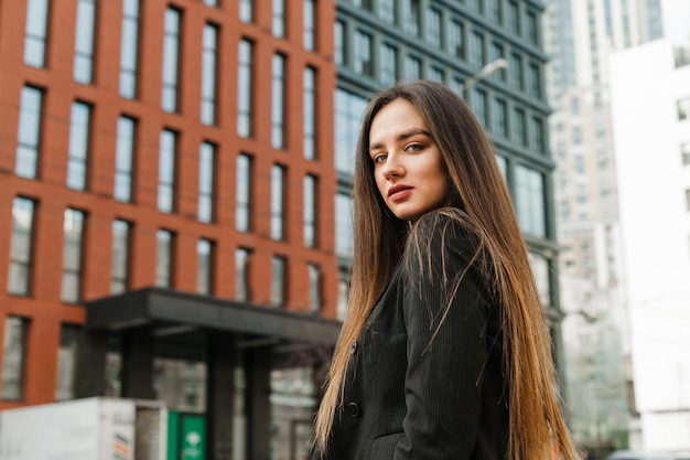 beautiful businesswoman in black jacket posing at camera on cityscape background