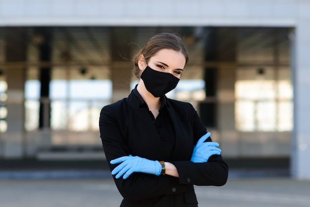Beautiful businesswoman in a black suit in a black medical mask and gloves at the city in quarantine and isolation. Pandemic COVID-19. Selective focus