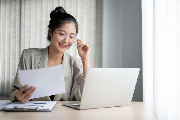 Photo a beautiful businesswoman is touching her eyeglasses while reading an online report on her laptop