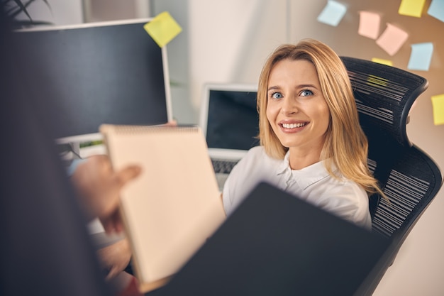 Beautiful businesswoman looking at coworker and smiling while handing him papers in office