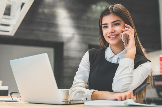 The beautiful businesswoman phones near the modern laptop