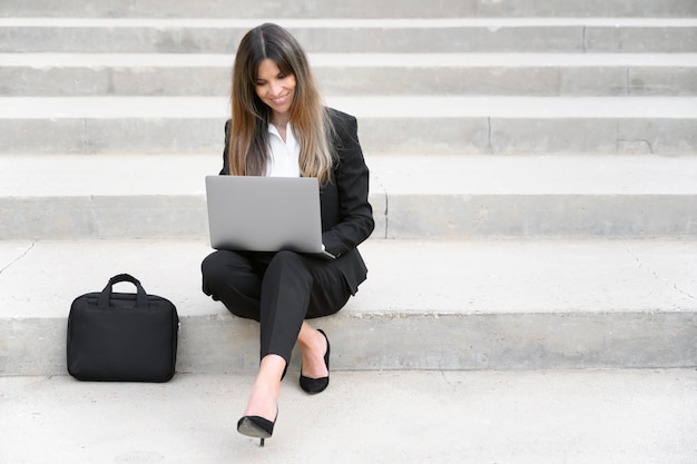 Beautiful businesswoman using laptop while sitting on stairs outdoors