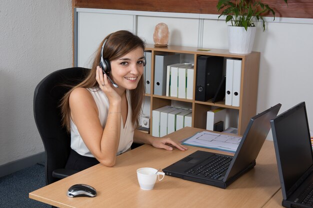 Bella donna d'affari con le cuffie lavorando alla scrivania