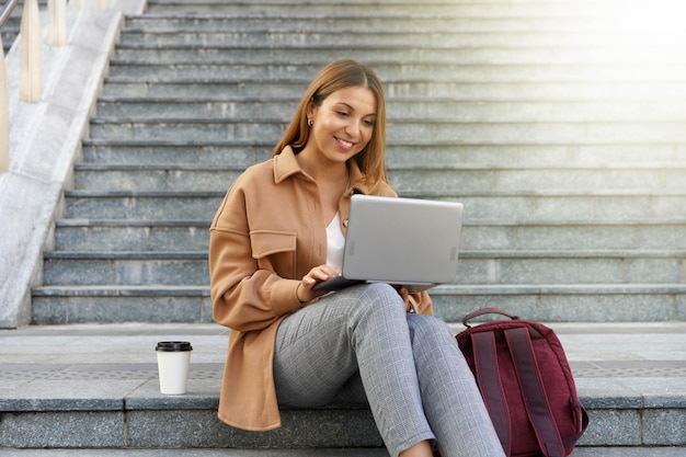 Beautiful businesswoman with laptop sitting on stairs outdoors