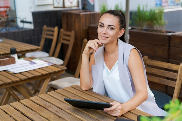 Beautiful businesswoman with smile sitting with touchpad in cozy restaurant while relaxing outside