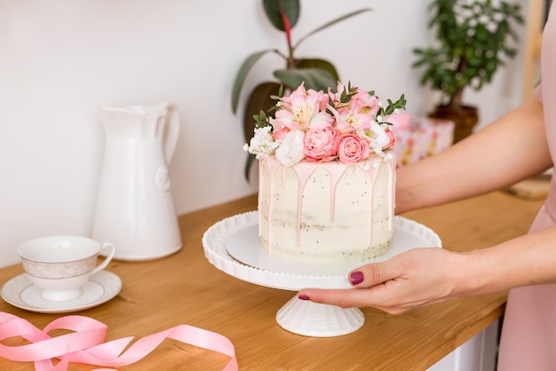 Bella torta con fiori su un supporto bianco nelle mani delle donne