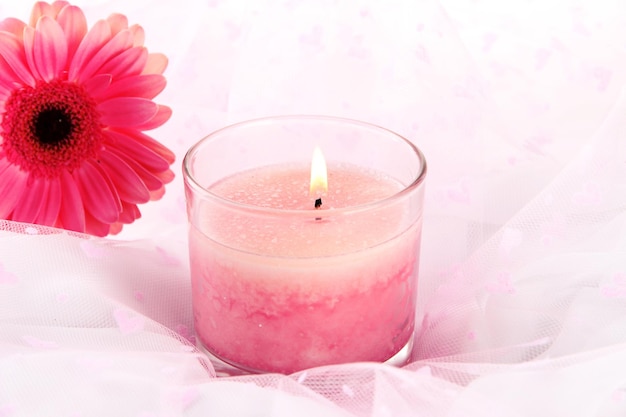 Beautiful candle with flower on white cloth, close up