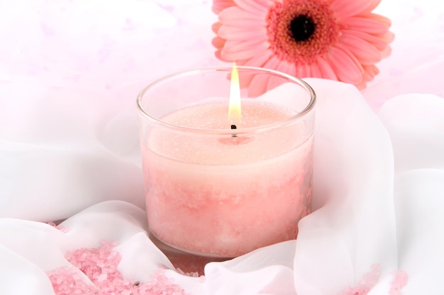 Beautiful candle with flower on white cloth, close up