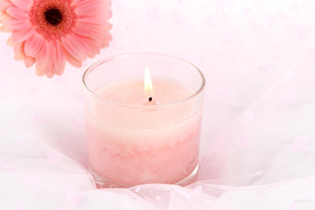 Beautiful candle with flower on white cloth, close up