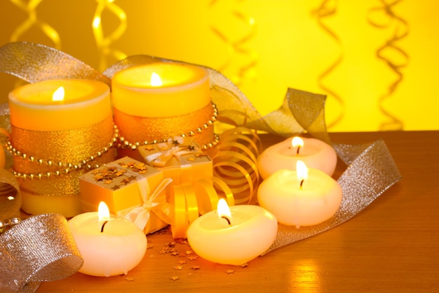 Beautiful candles, gifts and decor on wooden table on yellow background